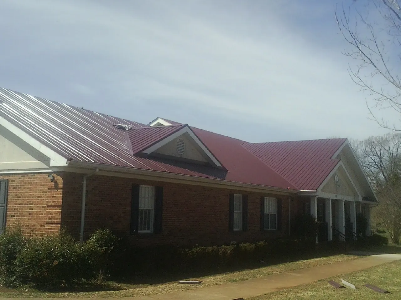 Red metal roof with gabled entries on a long brick building, from a Hail Damage Roof Repair job in Whitewater