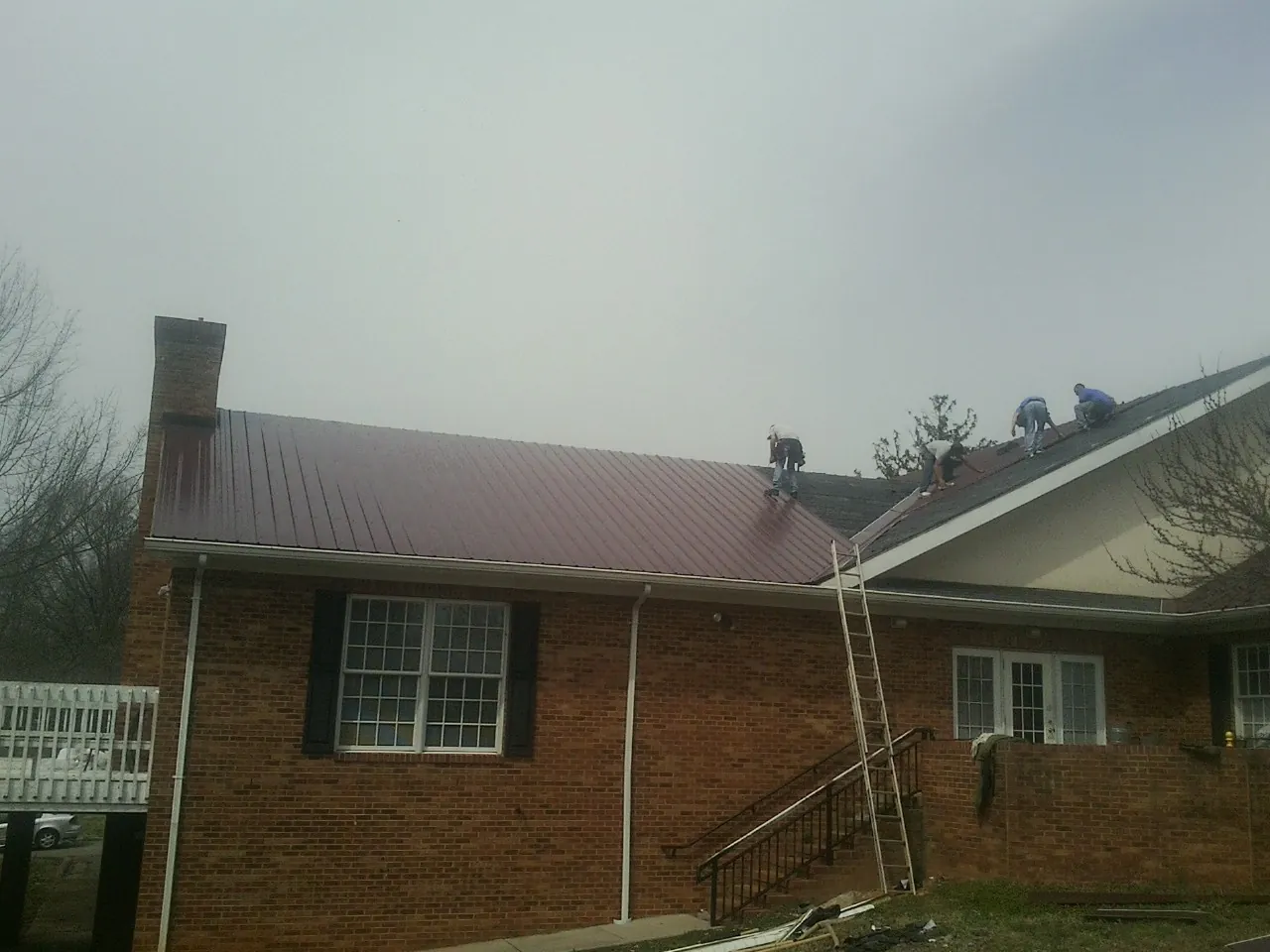 Crew setting red metal roofing panels on a brick home in Whitewater