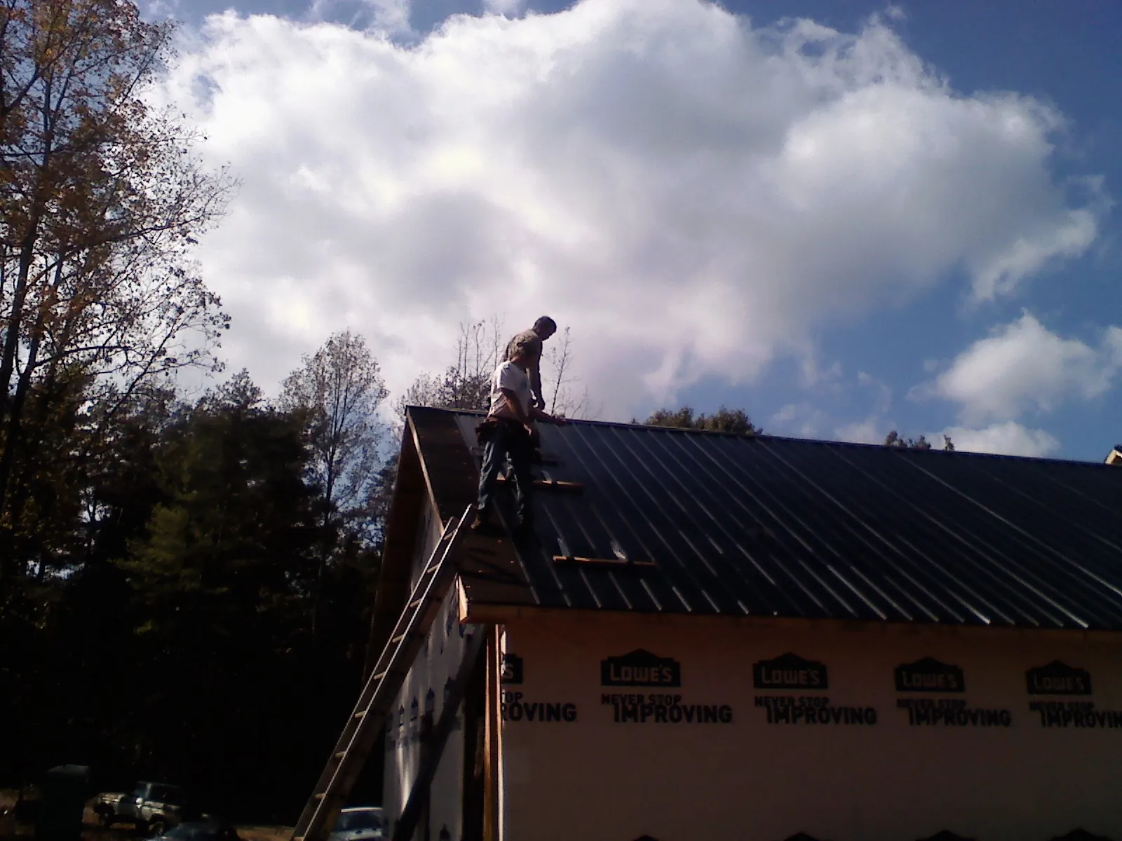 Roofer fastening dark metal panels high against a cloudy sky, from a Roof Inspection job in Whitewater
